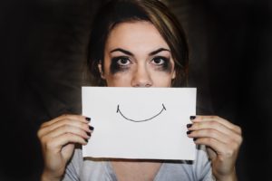 Une femme battue au foyer esquissant un sourire sur du papier placé sur sa bouche.